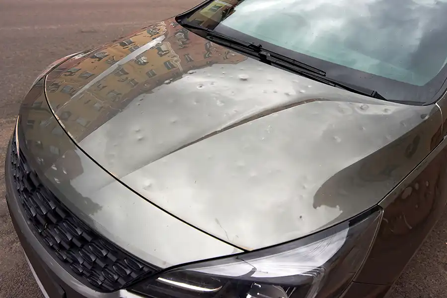Close-up of a car hood showing dents from hail damage.