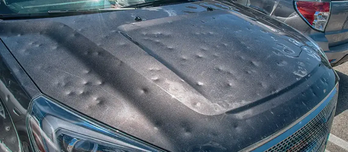 Close-up of a car hood with visible hail damage dents.
